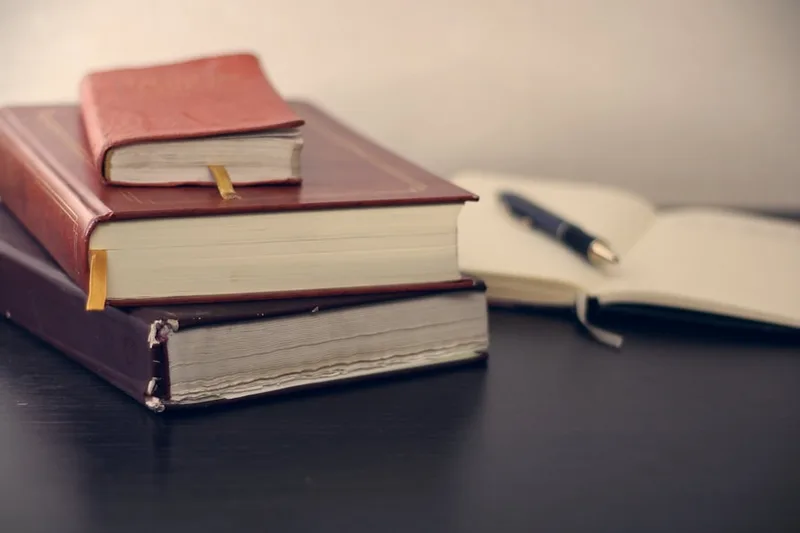 trabalhador brasileiro em home office estudando livro de finanças sobre “O que é alfabetização financeira (e o que não é)” com cofrinho e mo