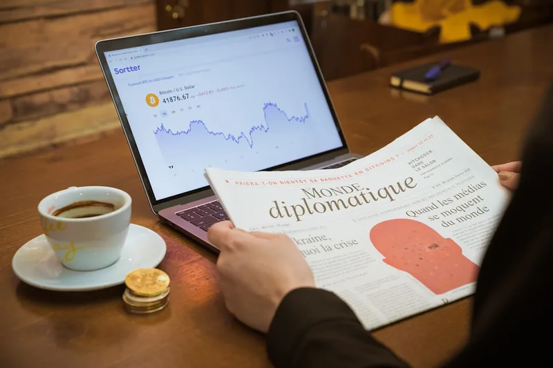 profissional liberal brasileiro lendo notícia econômica no tablet sobre “Exemplo numérico com R$ 450,00 por mês” com caneca e notebook em so