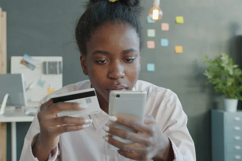 mulher brasileira jovem bloqueando cartão no aplicativo sobre “Como mapear sua situação atual em reais” com dois cartões lado a lado em café