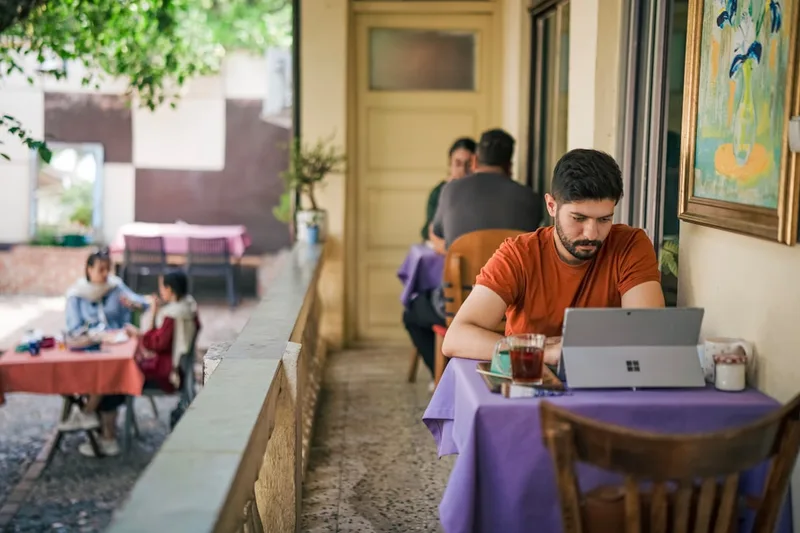 estudante universitário brasileiro checando app de notícias sobre “Exemplo numérico com R$ 290,00 por mês” com caneca e notebook em área de